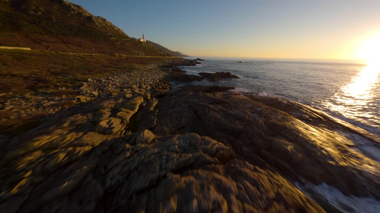 FPV drone flying along the Atlantic coast of Galicia at golden hour with waves and a Lighthouse