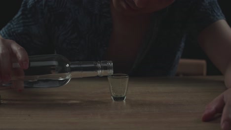 술에 취한 아시아인 남자가 술을 마시기 전에 글라스에 보드카를 부어 검은 바탕에서 잠을 자고 있습니다.