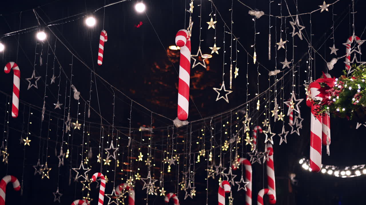 Bright red and white candy canes hang among twinkling stars and lights at a holiday market. Visitors enjoy the cheerful decorations while celebrating the season