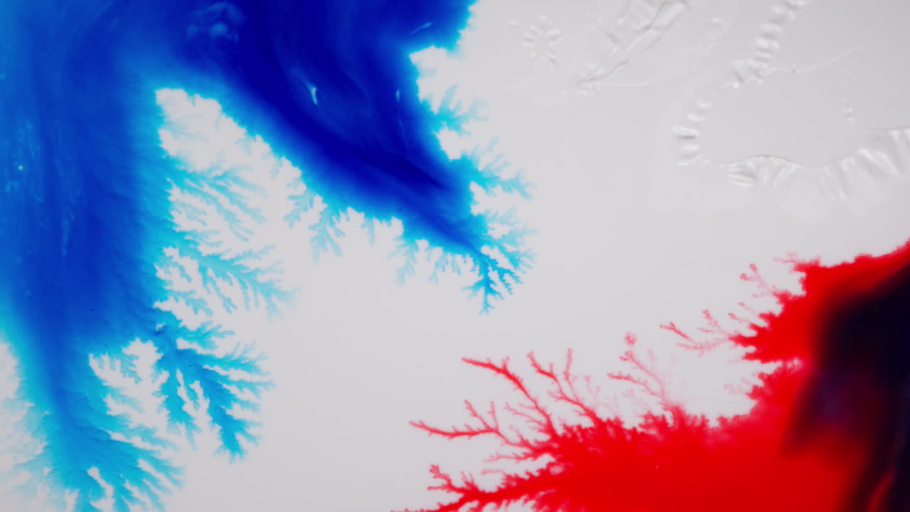 Abstrakcyjne makro niebieskiego i czerwonego atramentu w technice fluid art na białym tle.
