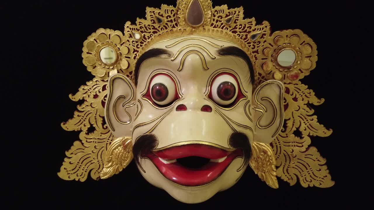 máscara de mono topeng tallada en madera, primer plano de la cara arte tradicional de bali indonesia, fondo infinito negro, adornos dorados