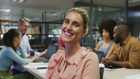 Portrait-of-caucasian-businesswoman-smiling-over-diverse-business-colleagues-talking