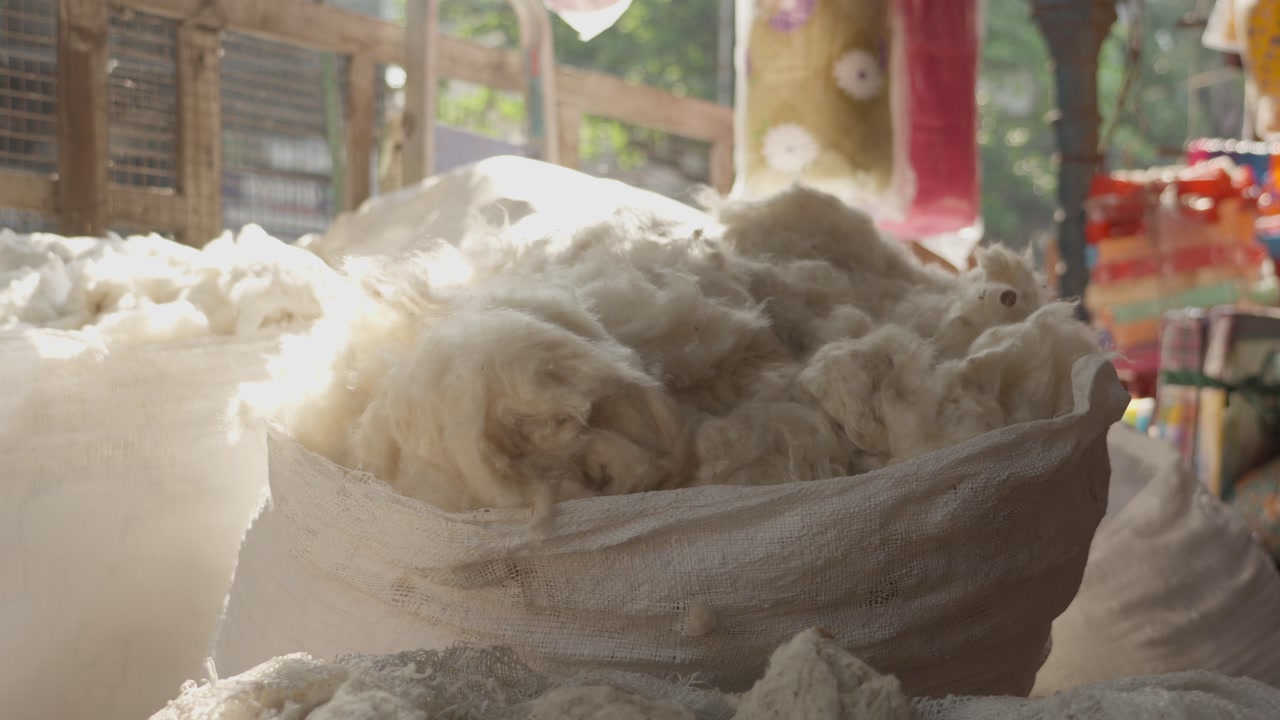 Close up of raw white cotton wool stored in large woven sacks at an outdoor market in Kolkata, India. Ideal for textile industry and trade concepts.