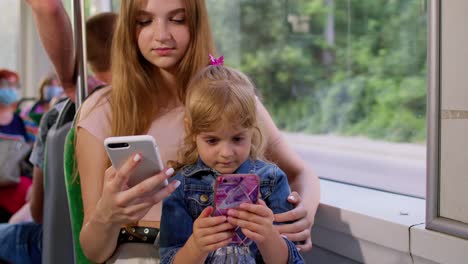 Child-girl-with-mother-using-smartphone-chatting-texting-in-social-media,-public-transport-bus,-tram