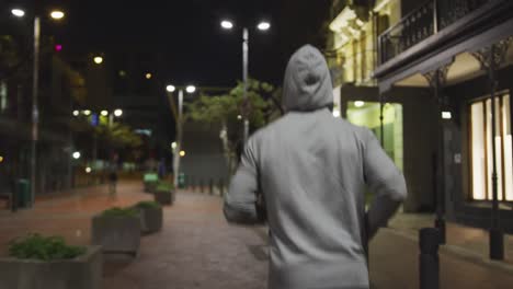 hombre con capucha caucásico haciendo deporte en una calle por la noche