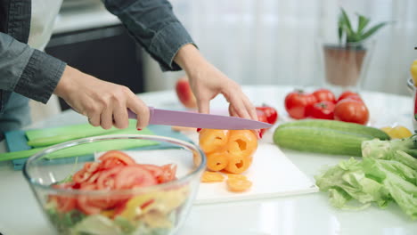 mujer cortando pimientos con un cuchillo afilado en la cocina. manos de primer plano cortando pimientos