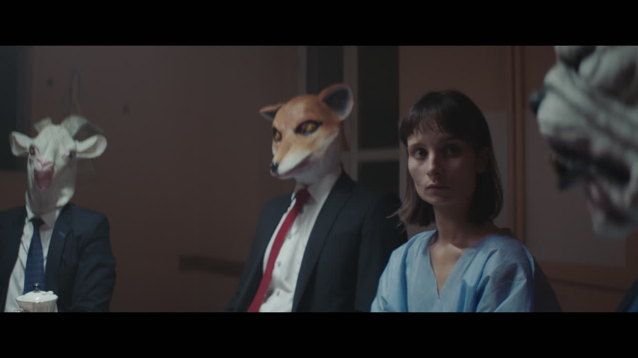 A girl sits at a table with strange figures in animal masks