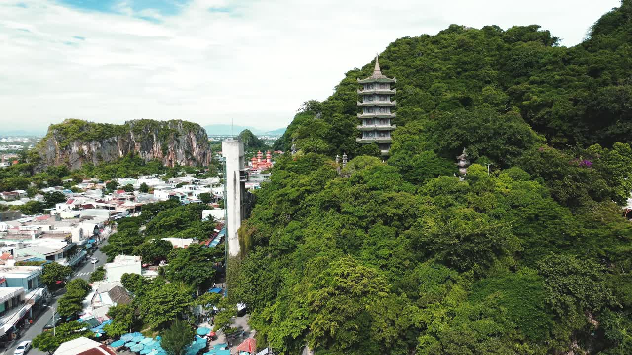Tall green hills and white pagoda in Da Nang Marble Mountains, Vietnam, daytime aerial establish