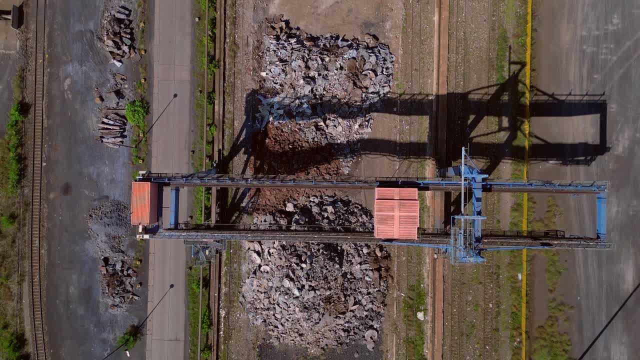 Gantry crane transporting scrap metal at Hennigsdorf electric steel mills on a sunny summer day. Breathtaking aerial view flight vertical bird's eye view drone