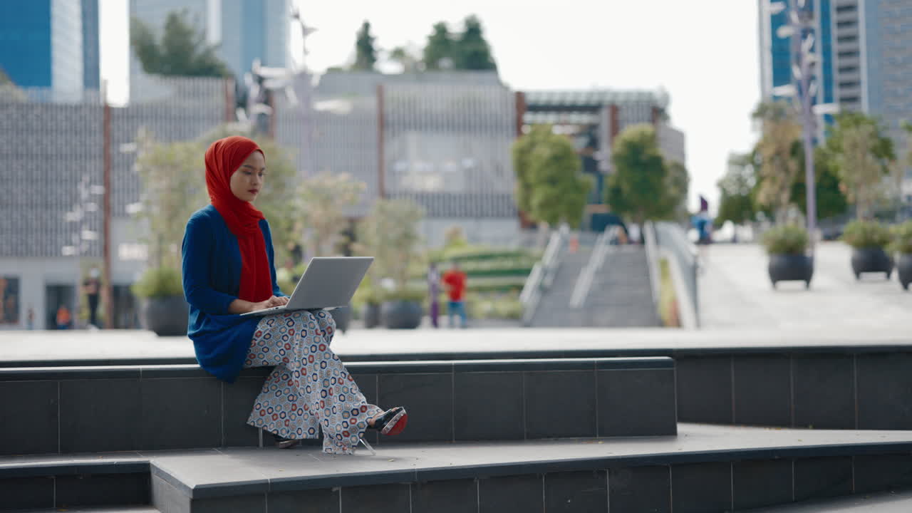Young Woman in Hijab Working on Laptop Outdoors in Urban Setting