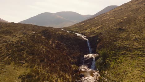 Aerial drone footage of a scenic river flowing through the rugged landscape of the Isle of Skye, featuring a beautiful waterfall surrounded by dramatic hills and untouched nature