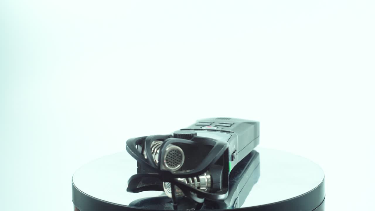 um close-up de um prático gravador de áudio de bolso, estéreo de som preto, em um suporte giratório refletivo 360, porta de entrada e saída de linha, botões de volume, câmera lenta, vídeo 4k