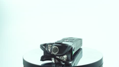 a close up shot of a handy pocket audio recorder, black sound stereophone, on a reflecting 360 rotating stand, line in and out port, volume buttons, slow motion, 4k video