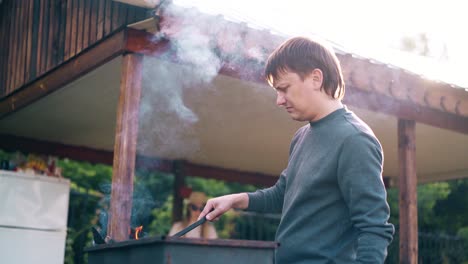 young man standing near the summer house prepares the coals in the grill the girls help him