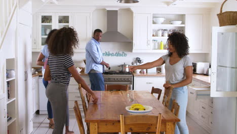 family with teenage children laying table for meal in kitchen