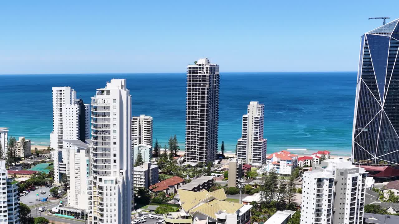 Drone ascends above Broadbeach Waters, revealing modern skyscrapers, coastline, and clear blue sky