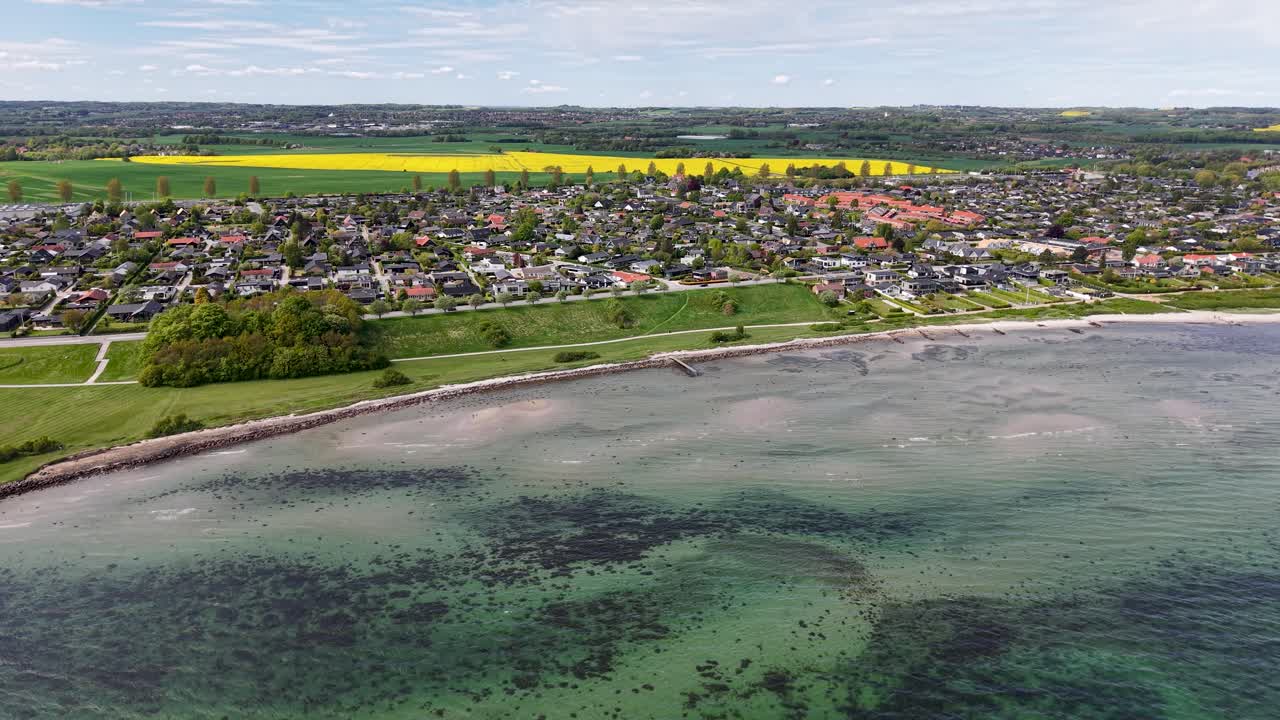 Aerial drone view of a Danish coastal neighborhood with shallow turquoise waters and a tree-lined shoreline near Aarhus