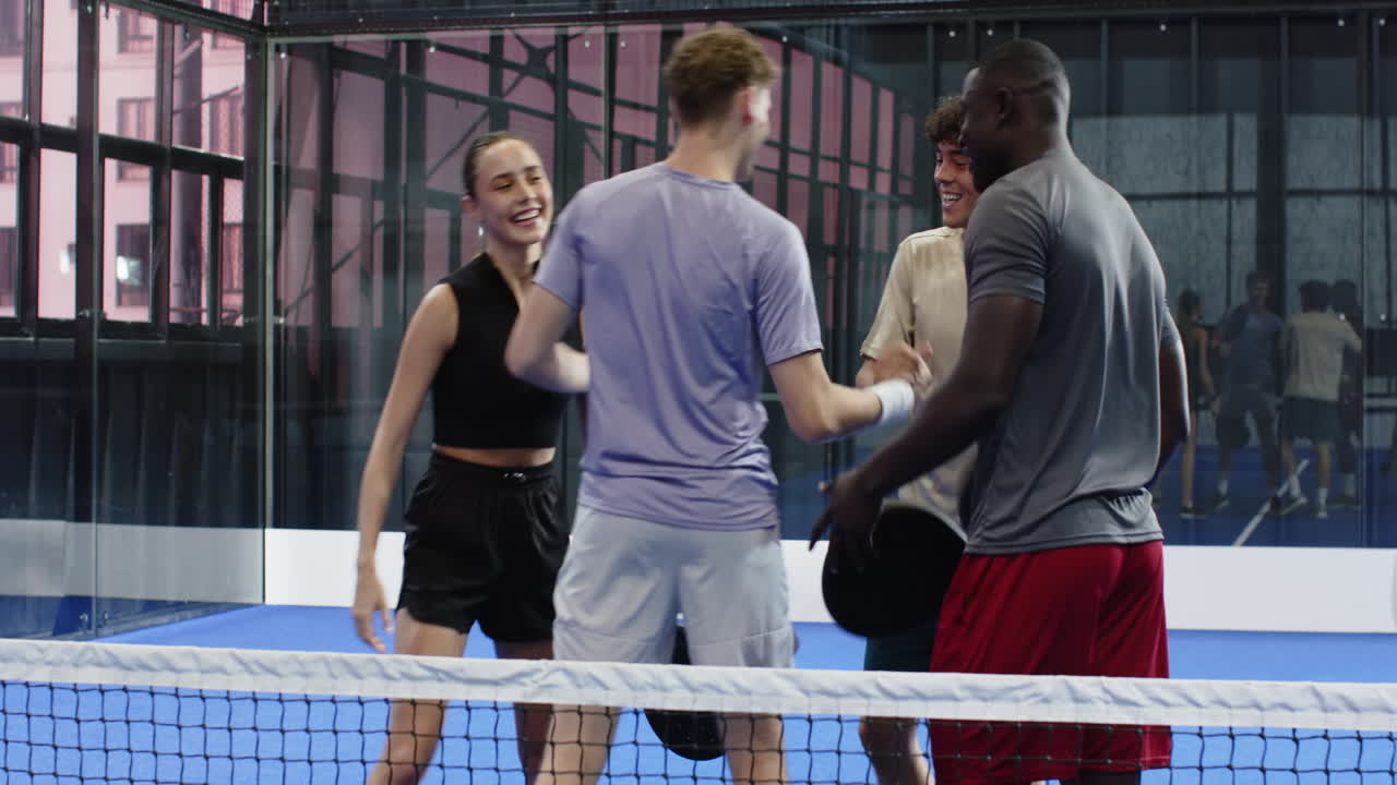 Diverse friends enjoying padel tennis match, laughing and chatting on court, on indoor court