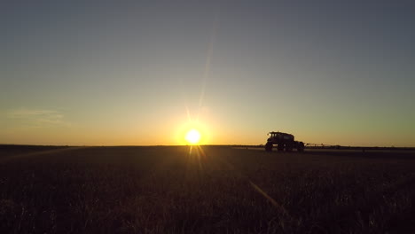 Eine-Sprühtraktormaschine-Gegen-Pulsierendes-Sonnenlicht-Während-Des-Sonnenuntergangs,-Die-Herbizide-Auf-Den-Feldern-Anwendet