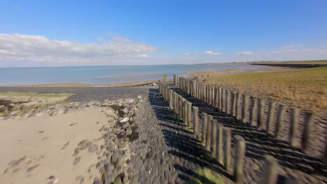 Aerial-drone-flight-along-wooden-wave-breakers-at-empty-beach-in-daylight