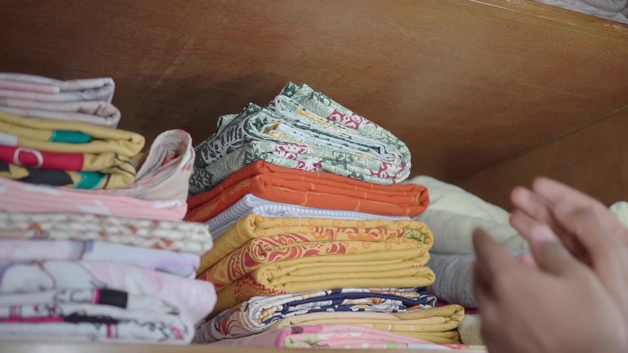 Person Organizing Folded Bed Sheets and Towels in a Wooden Closet