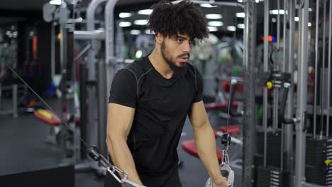 joven haciendo ejercicio en una estación múltiple en el gimnasio para los músculos de los brazos y los hombros