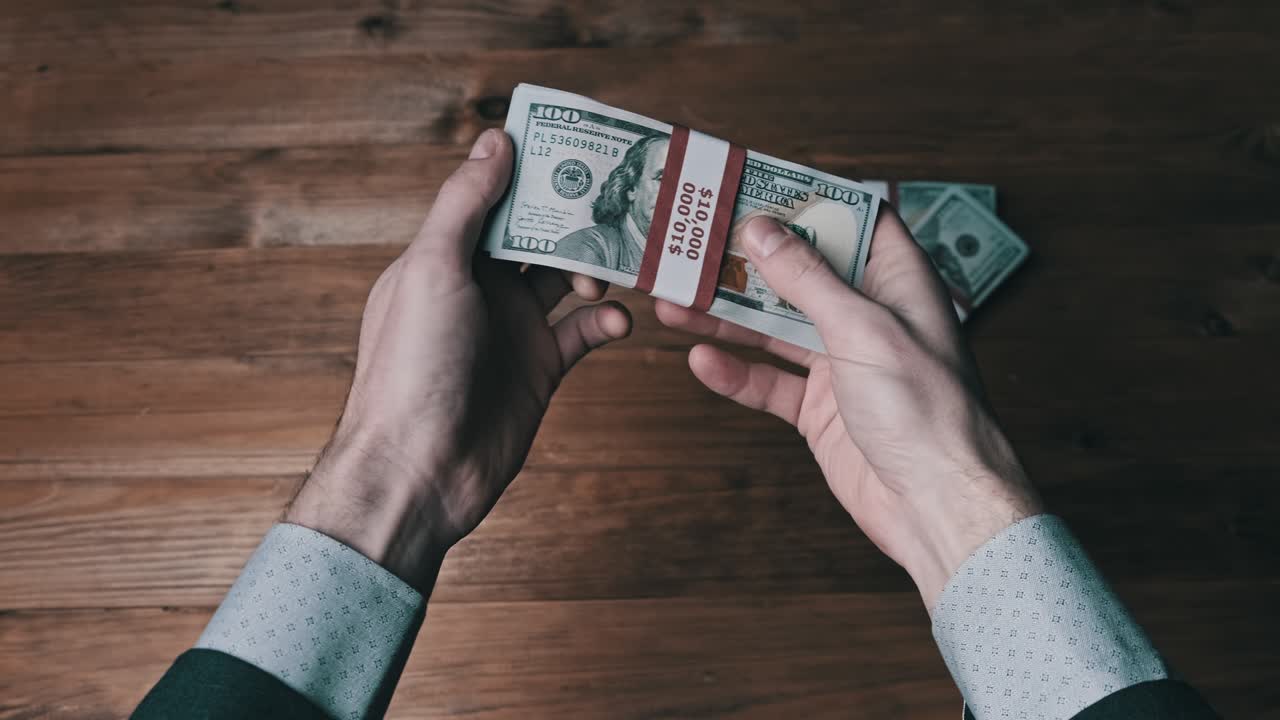 una pila de billetes de 10.000 dólares estadounidenses en manos masculinas sobre un fondo de madera.