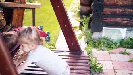 los niños en primer plano se balancean en un gran columpio de madera cerca de la casa de verano en la que juegan