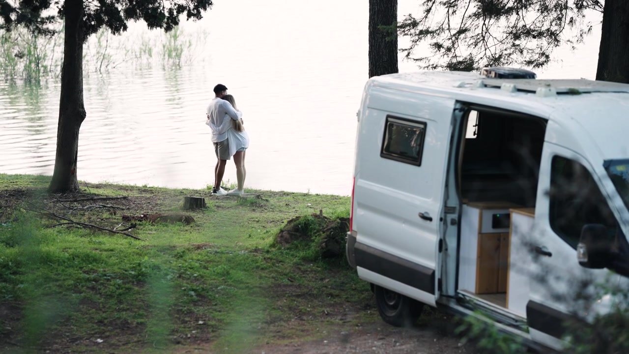 Young Couple Embracing by Lake Next to Camper Van