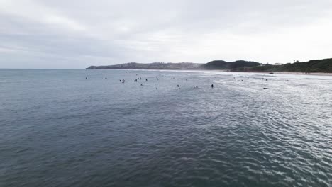 Toma-Aérea-De-Decenas-De-Surfistas-Nadando-Sobre-Grandes-Olas-En-Playa-Meron-En-San-Vicente-De-La-Barquera