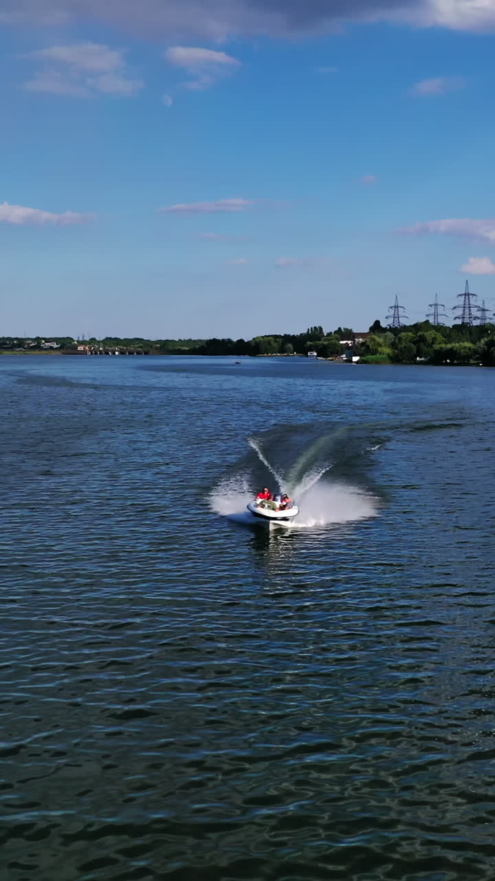 Boat sailing in the river. People travel in motorboat on the background of high voltage electric lines in summer. Aerial view. Vertical video