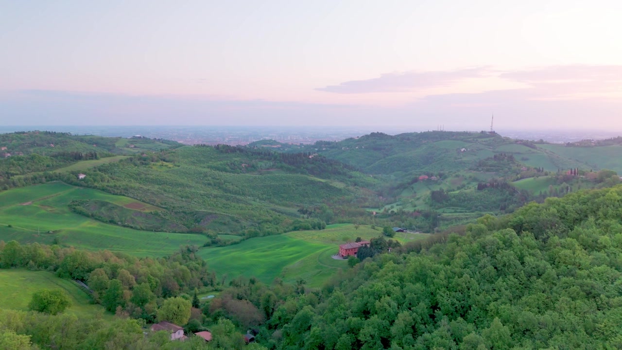 Drone che si alza all'alba sopra il Parco di Forte Bandiera sul Monte Donato, rivelando colline verdi, foreste e la lontana Bologna mentre la telecamera ruota a semicerchio