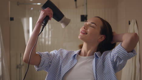 joyful woman using hairdryer in bathroom closeup. happy girl dancing at home