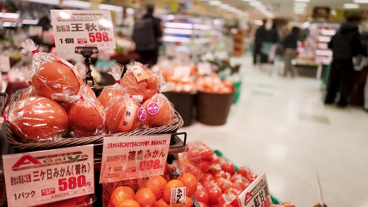 明るい日本の食料品店の棚に並べられた、パッケージされた梨とオレンジの静止画クローズアップショット。