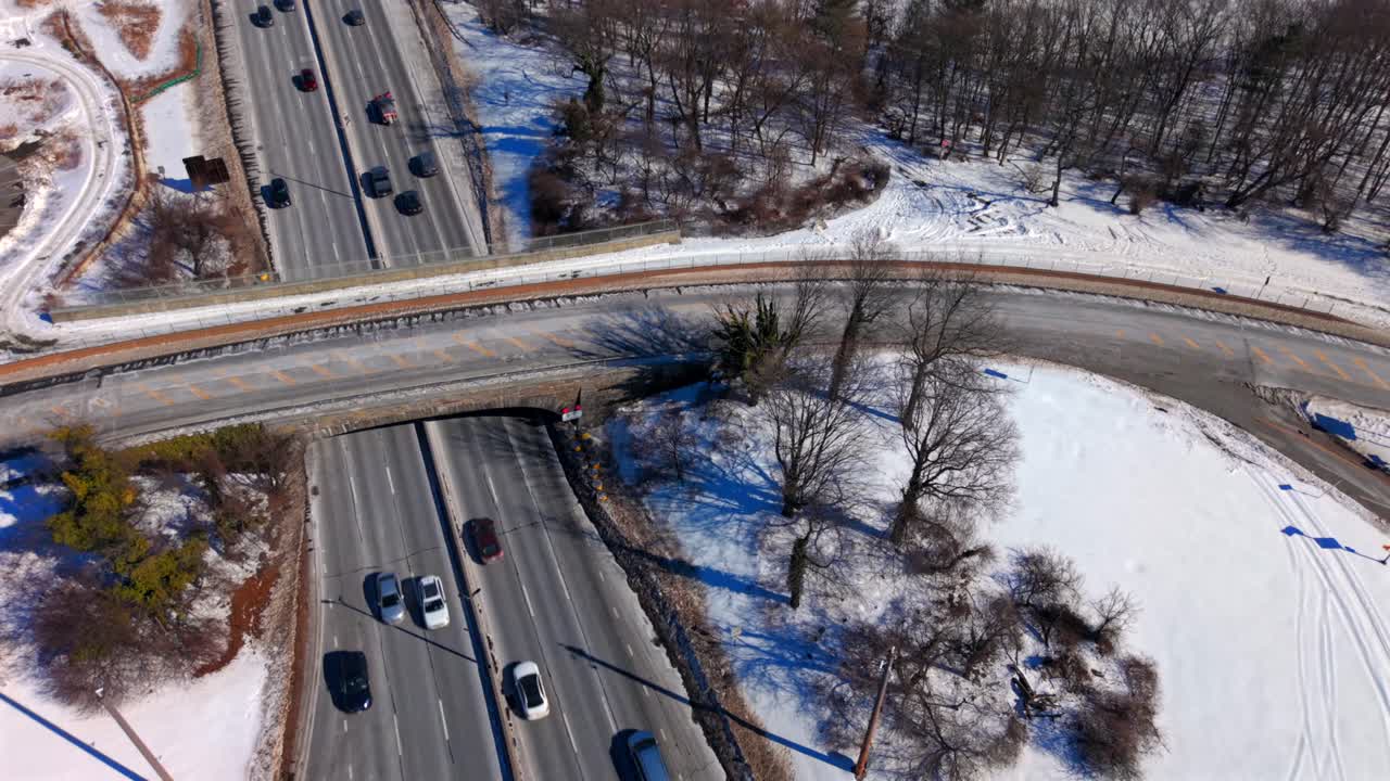 Luftaufnahme einer Überführung auf dem Southern State Parkway an einem sonnigen Tag mit Schnee am Boden. Die Kamera neigte sich nach unten, fuhr heraus und neigte sich wieder hoch, während Fahrzeuge in der winterlichen Landschaft vorbeifuhren.