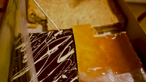 a woman hand is cutting various cake such as apple pie, poppy seed cake and cheese cake bought from local shop during christmas celebration in a large box.