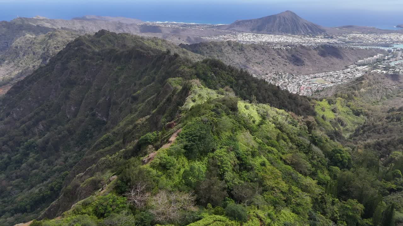 Drone flying above the high mountain peaks on Oahu, Hawaii, with the ocean at distance. Dramatic tropical mountains and scenic island coastline