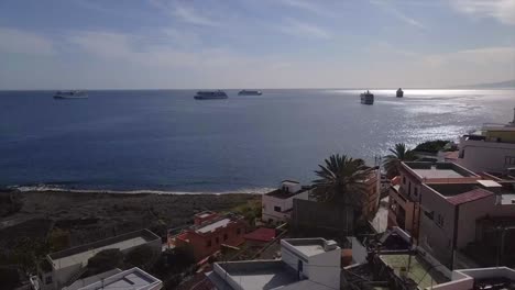 dolly aérea cinematográfica delante de la aldea costera en el mar azul, grandes barcos en el fondo, tenerife, españa