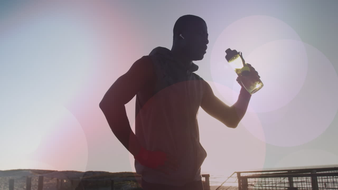 manchas coloridas de luz contra afroamericano hombre en forma bebiendo agua en la playa