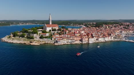 Vista-Aérea-Mientras-Un-Barco-Sale-Del-Casco-Antiguo-De-Rovinj,-Famosa-Ciudad-Medieval-Croata-En-El-Mar