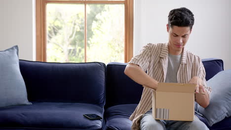 happy biracial man opening delivery in cardboard box and using smartphone, copy space, slow motion