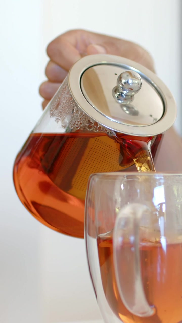 Video verticale: Mano che inclina una teiera con infusore, versando tè fumante in una tazza in cucina.