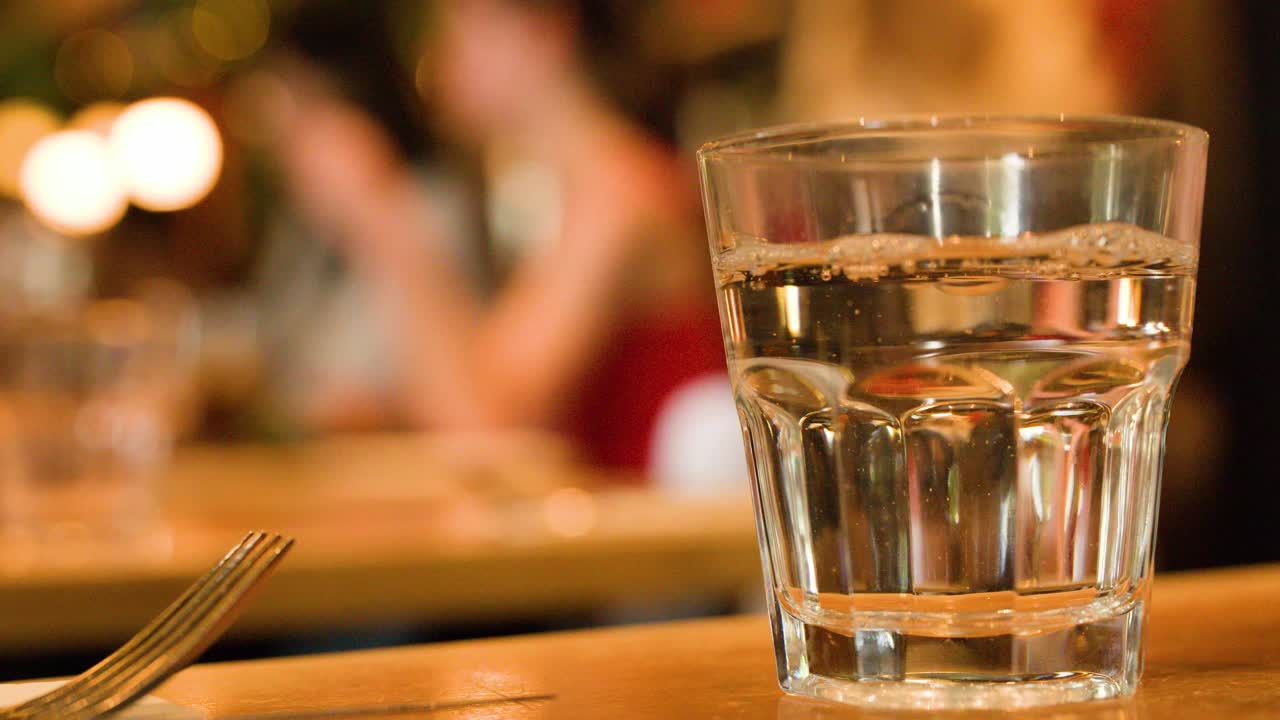 Close-up of water being poured into glass, warm ambient lighting, shallow depth of field
