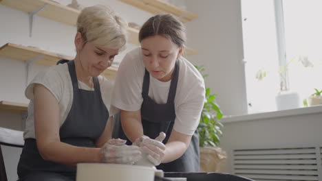 Caucasian-girl-teaches-an-elderly-puppy-to-work-on-a-potter's-wheel.-Assistance-in-the-rehabilitation-and-adaptation-of-pensioners.-Time-lapse-filming-of-an-elderly-woman's-potter's-wheel