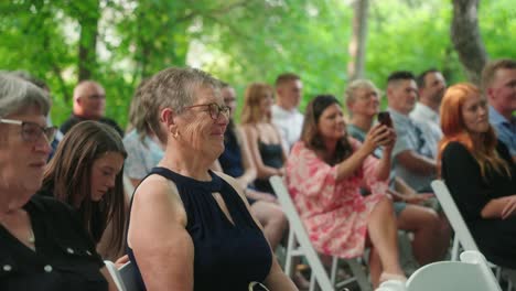 Grandmother in dark blue gown smiles in front row at outdoor wedding