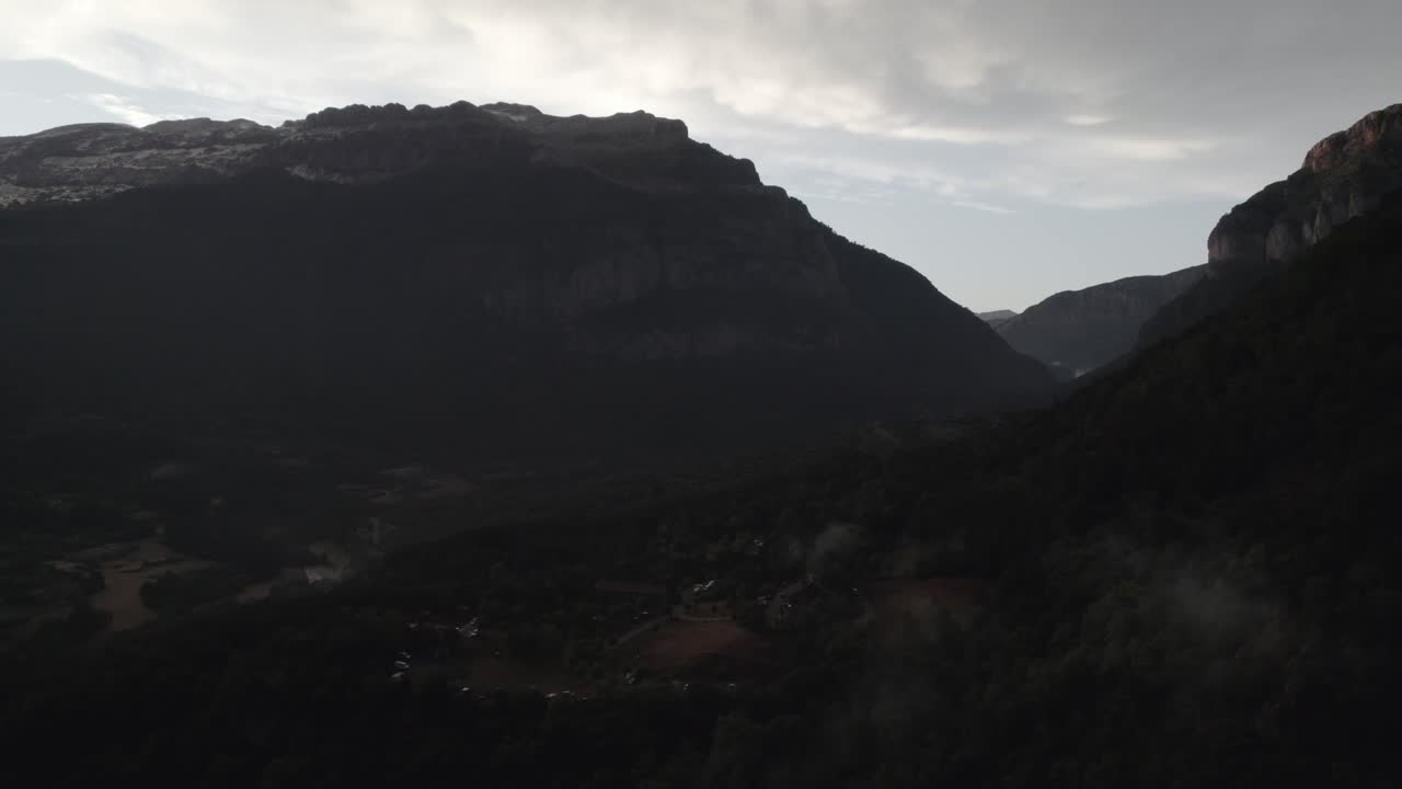 This drone video captures a breathtaking ascending crane shot over the Hecho Valley in the Aragonese Pyrenees, Spain, showcasing snowy mountains, a cloudy sunset, and the Borda Bisaltico campsite.