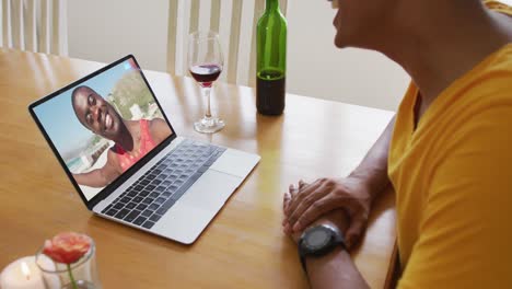 Mixed-race-man-sitting-at-table-using-laptop-making-video-call-with-male-friend