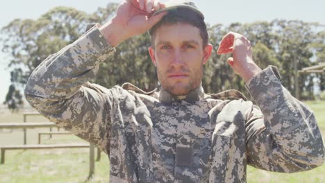 Portrait-of-caucasian-male-soldier-in-combat-uniform-and-cap-standing-on-army-obstacle-course