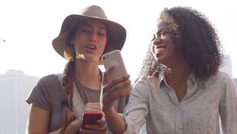 female friends look at photos on phone by manhattan skyline