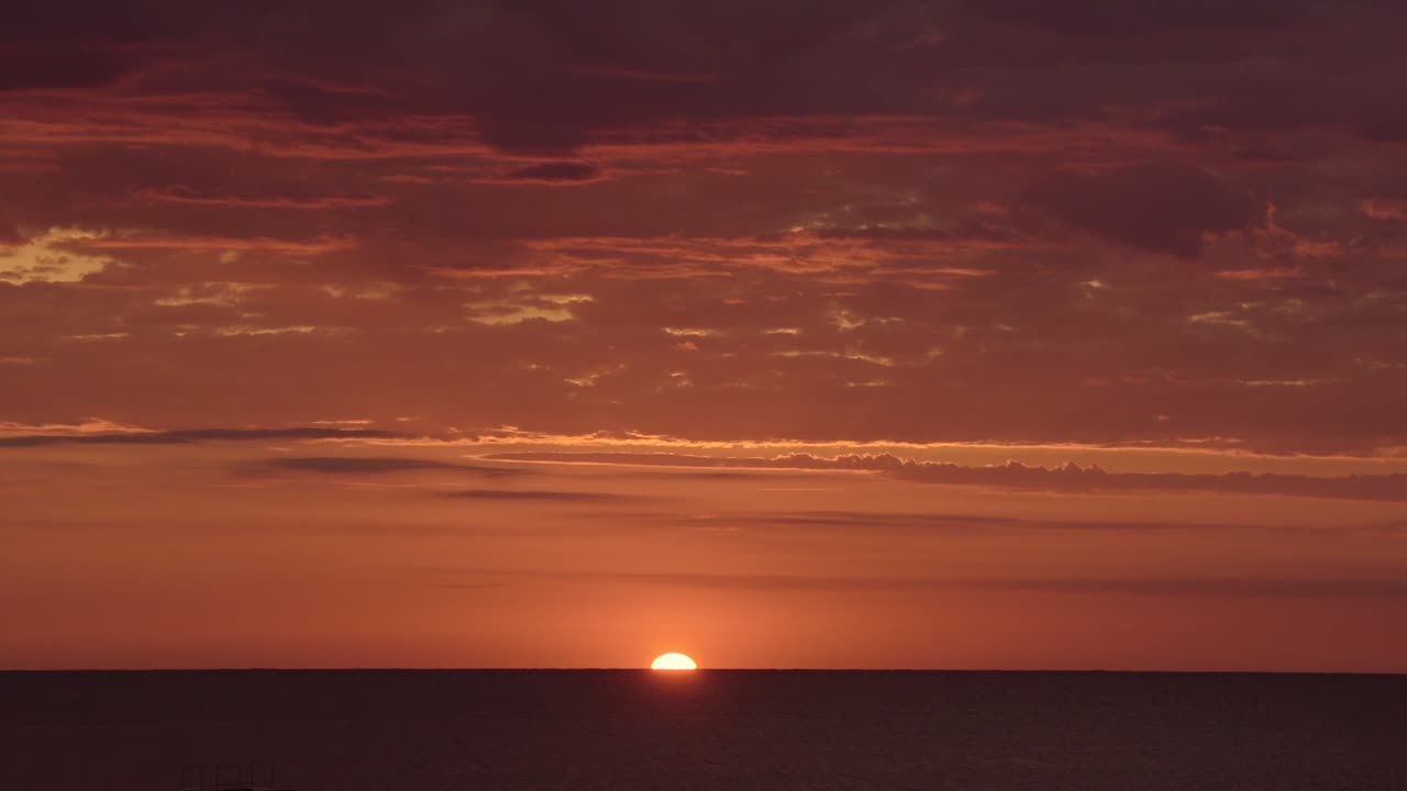 Sun going behind the ocean on a bright red and orange sunset, with few clouds
